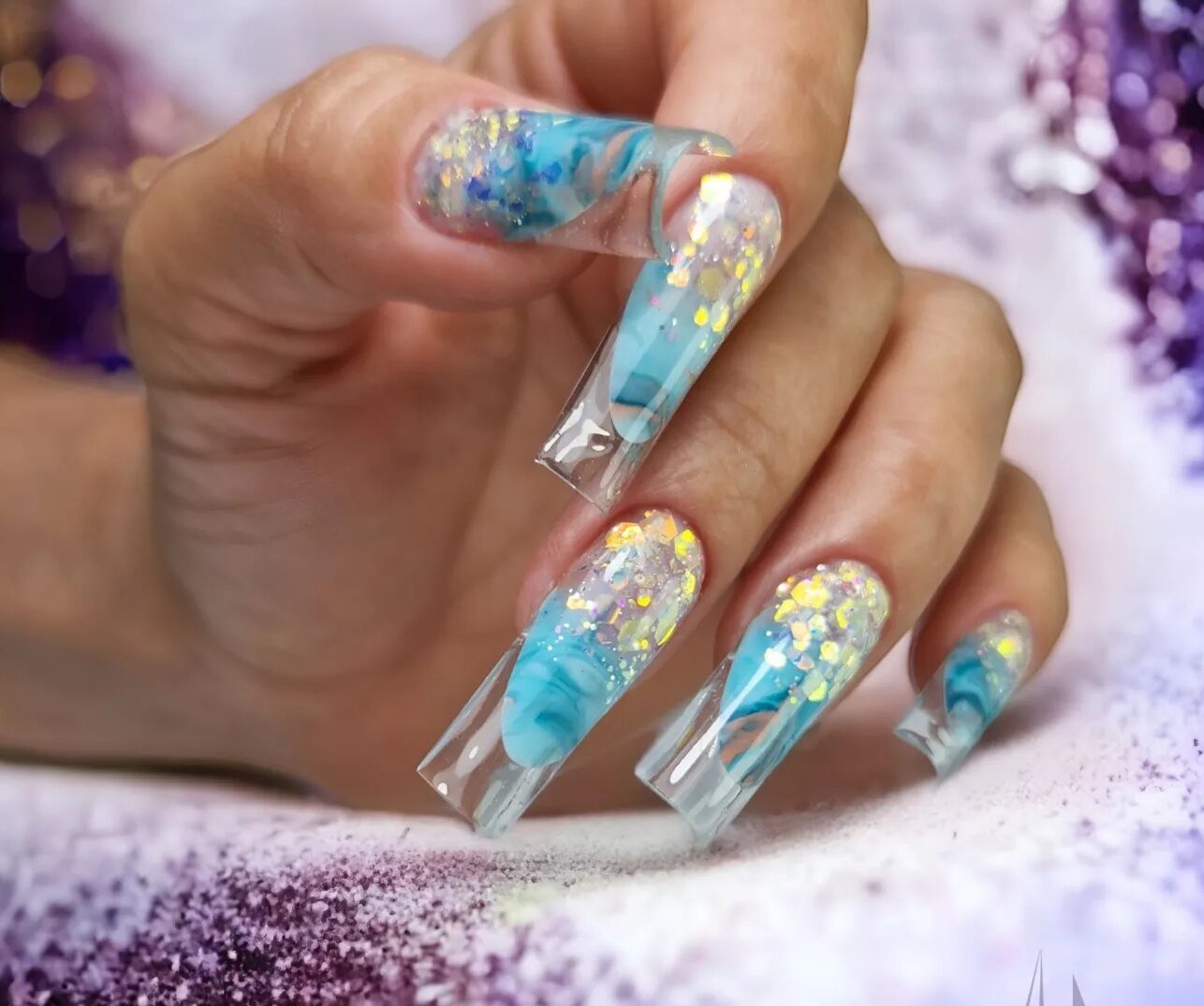 Long square shaped clear acrylic nails with blue marble nail design and gold glitters