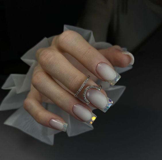 Long square shaped pale white nails with clear French tips and glitters