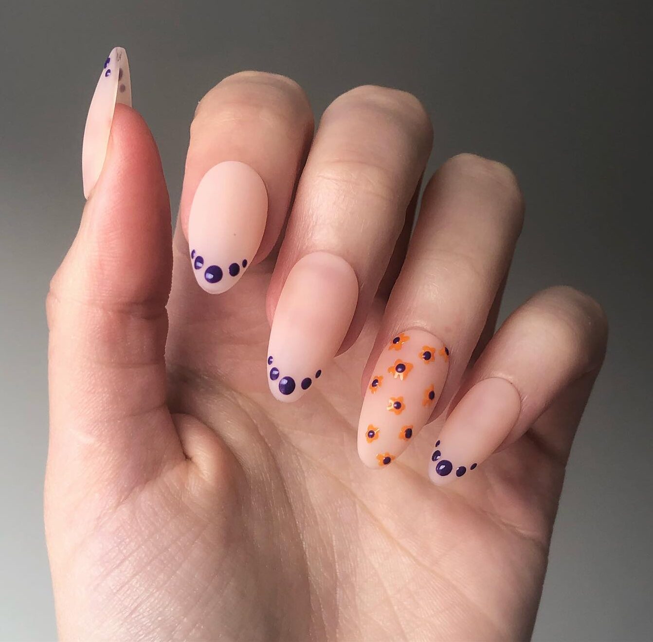 Neutral nail polish in matte finish with blue polka dots French tips and tiny flowers on long almond nails