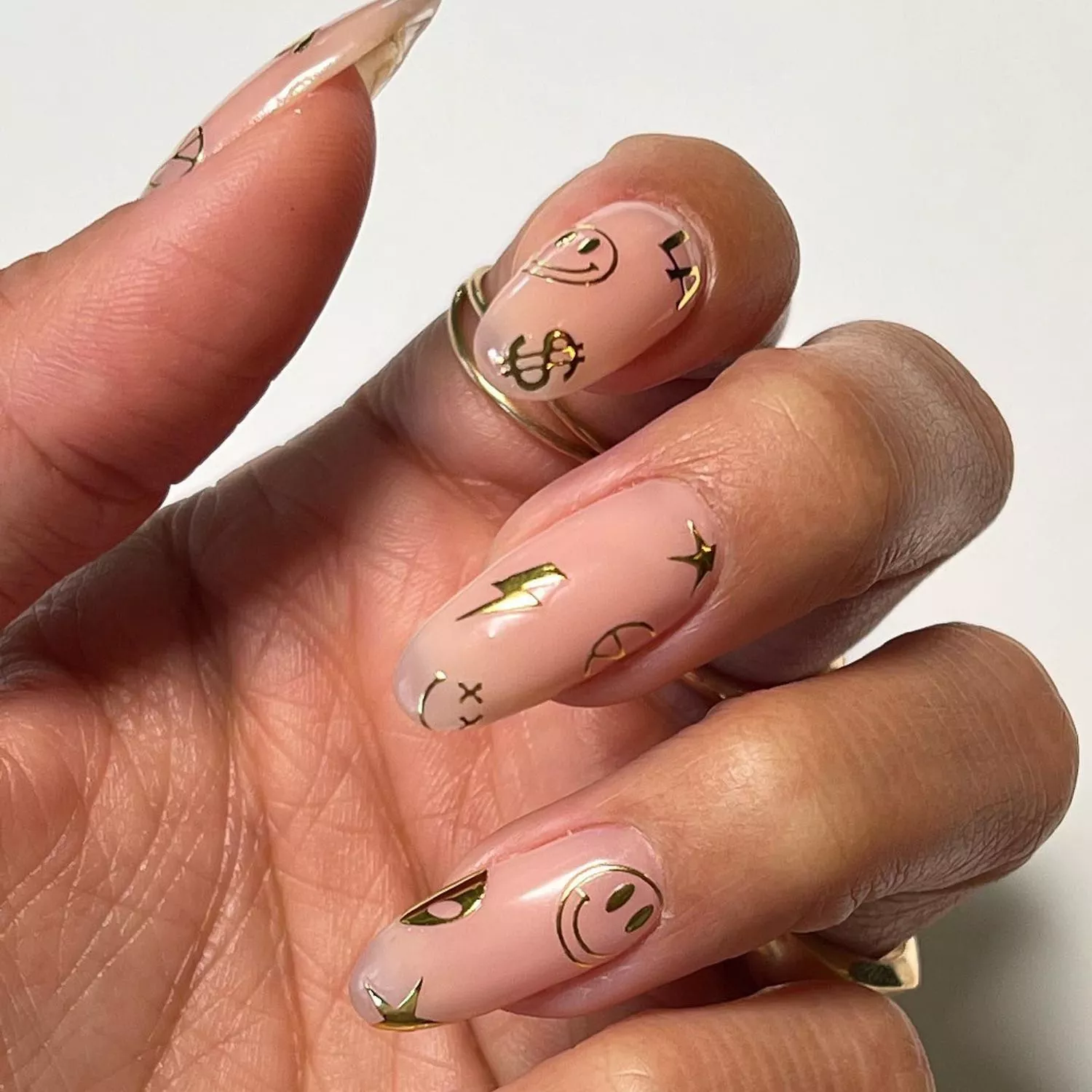 Manicure with neutral base and gold smiley, dollar sign, and lightning bolt stickers