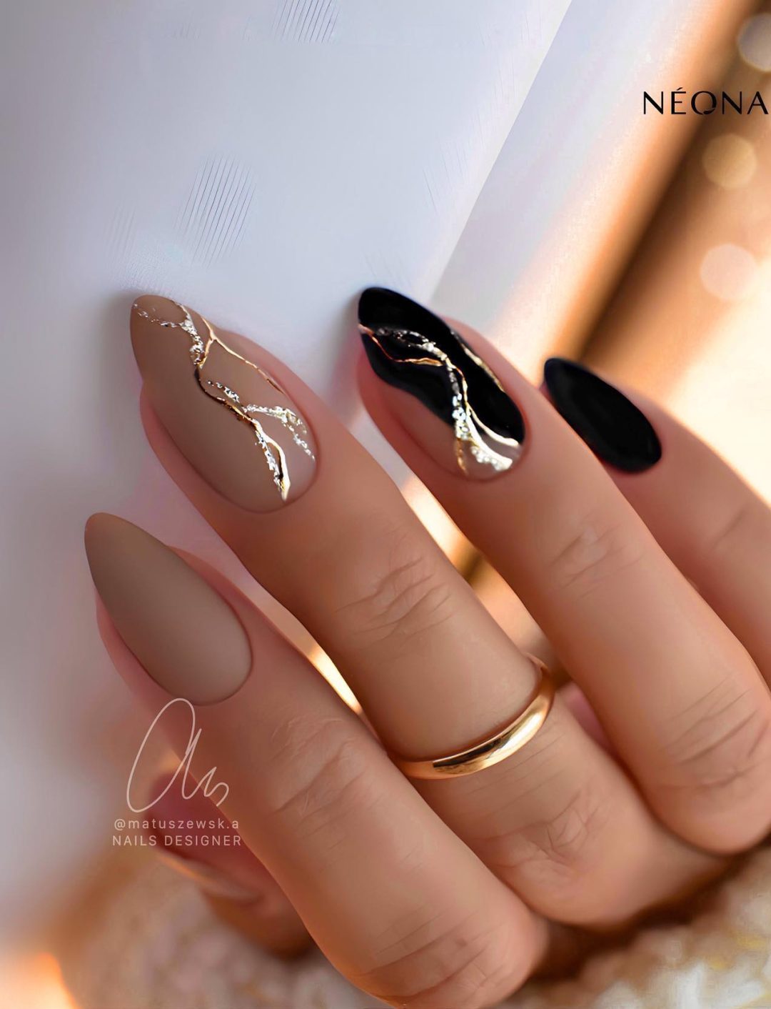 Matte beige and black nails with gold stripes.