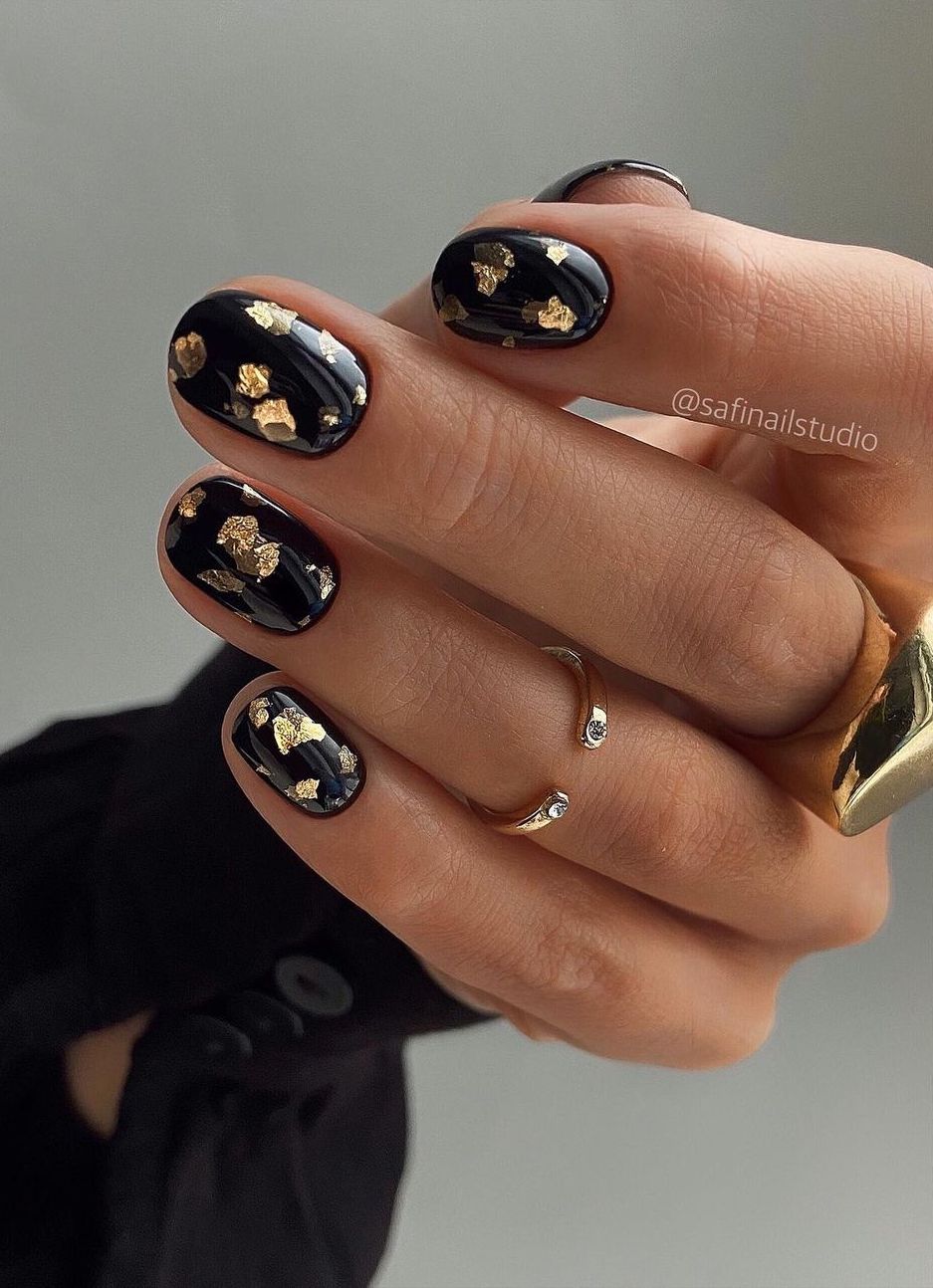 Short black nails with gold foil flakes.