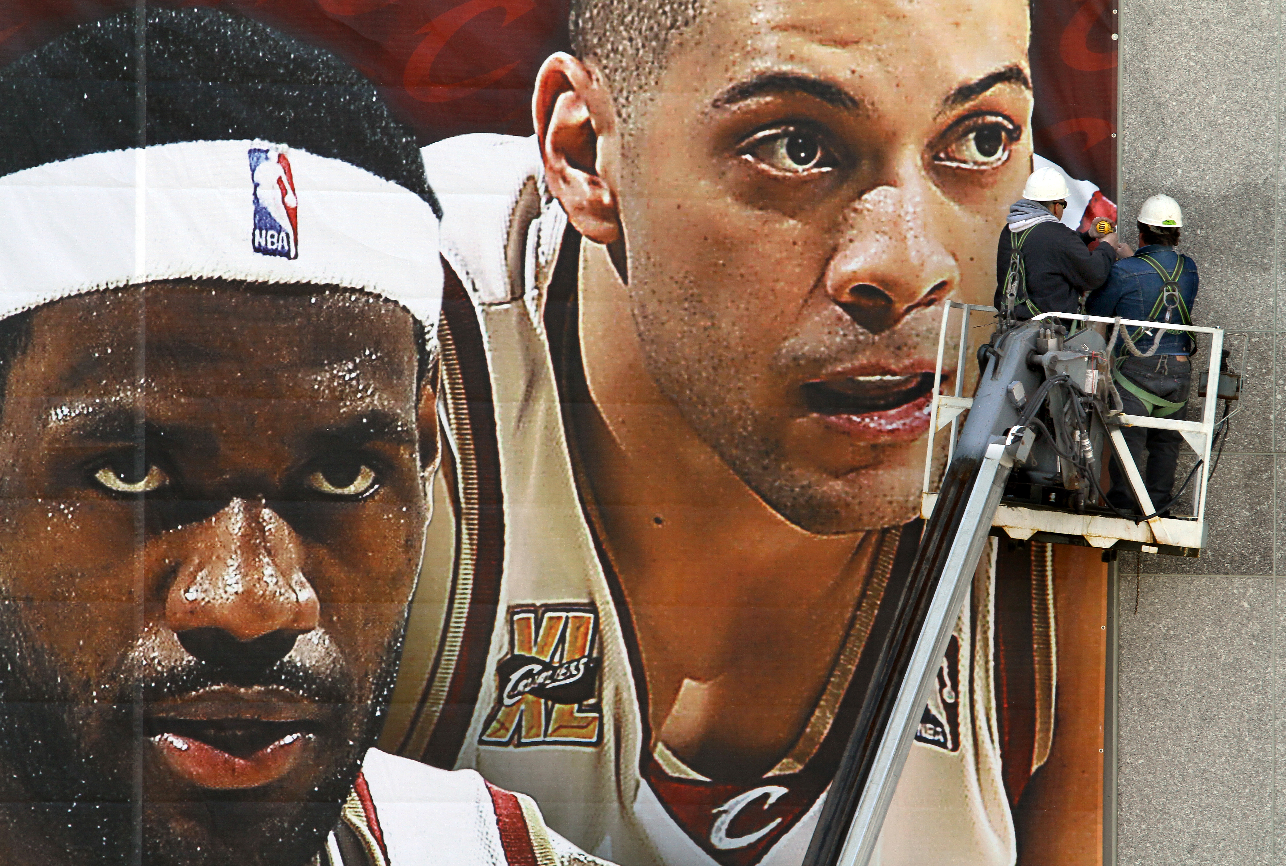 Carlos Vicens (cq), left, and Brian Shaffer, both employees of Boyer Signs   Graphics, Inc., are dwarfed by the faces of LeBron James and Anthony Parker as they drill the sides of one of the new Cavaliers 2010 playoff murals on the side of Quicken Loans Arena on Wednesday, April 14, 2010.  (Lisa DeJong/The Plain Dealer)