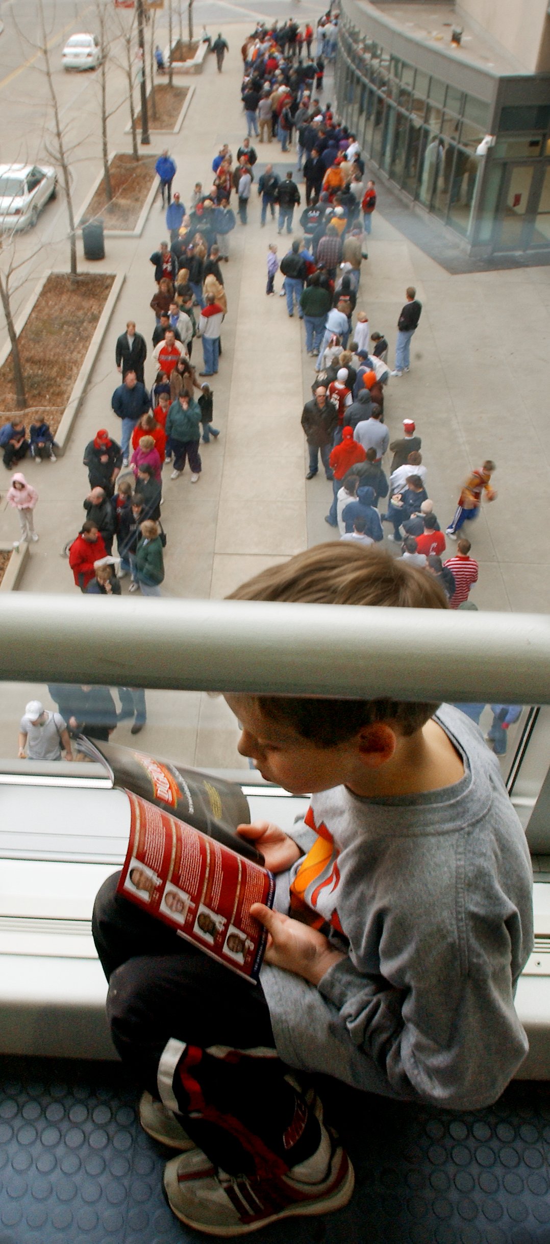 Nick butcher of Sandusky reads a Cleveland Cavaliers players program as he waits along with thousands of fans waiting to get their complimentary LeBron James bobble head souvenir March 3, 2004 outside the Gund Arena before the gates opened for tonight's game against the Atlanta Hawks.  Nick was picked up from school at 2:30pm had an hour drive to the arena and waited until shortly after 4:00pm in the garage walkway line. The picture was taken at 5 p.m. and the lines went around the Gund at least twice,  with 4 entrances. The bobblehead was given to the first 10,000 fans. The Gund holds about 17,000. (John Kuntz/The Plain Dealer)