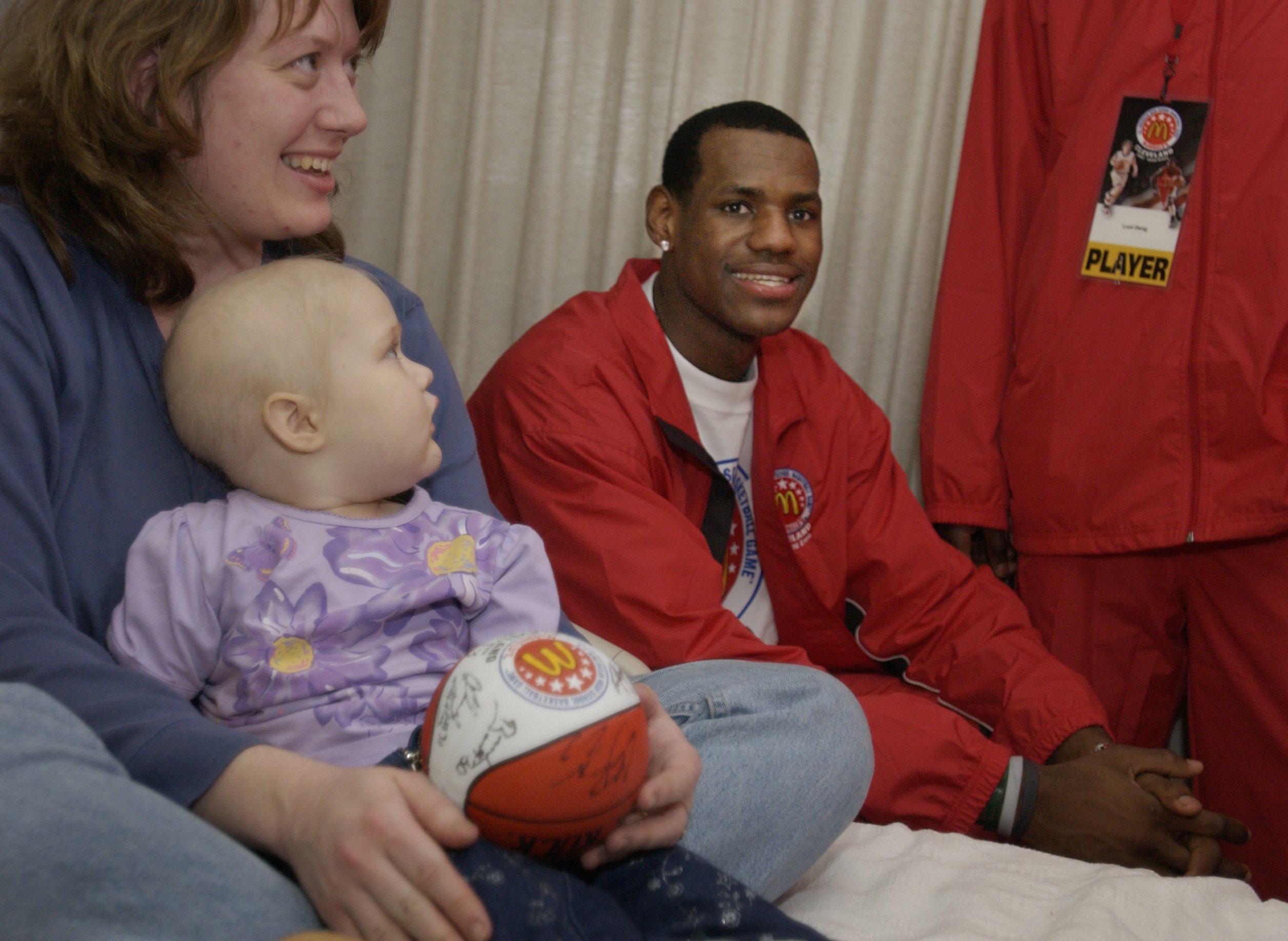 26-month-old Jesse Hyatt of Wooster and her mom, Joyce, got a surprise visit from a group of players that included local standout LeBron James, seated,  as groups of players toured Akron Children's Hospital Sunday afternoon.   While LeBron and Joyce enjoy a light moment, Jesse intently studies the tall players that invaded her room.  SUNDAY MARCH 23,2003 (BILL KENNEDY/PLAIN DEALER)